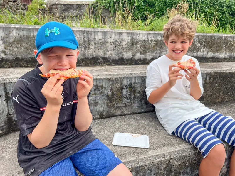 Zwei Kinder sitzen auf einer Steintreppe und essen Pizza