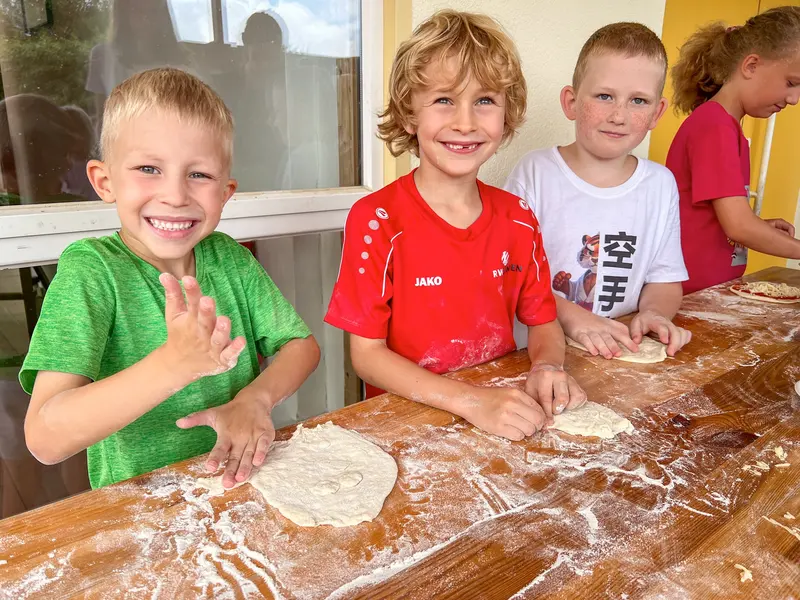 Drei Kinder stehen an einem Tisch und kneten Pizzateig