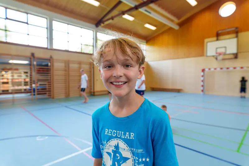 Kind steht lächelnd in einer Turnhalle