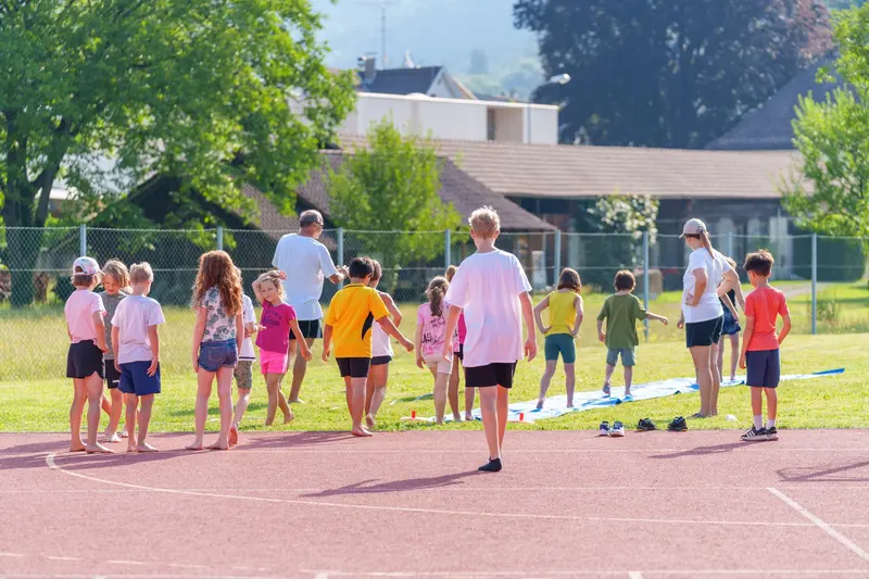 Kinder spielen ein Laufspiel auf einem Sportplatz, Erwachsener beobachtet