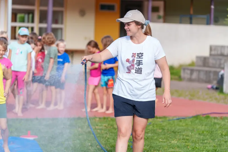 Erwachsener spritzt mit Schlauch Wasser über eine Reihe Kinder