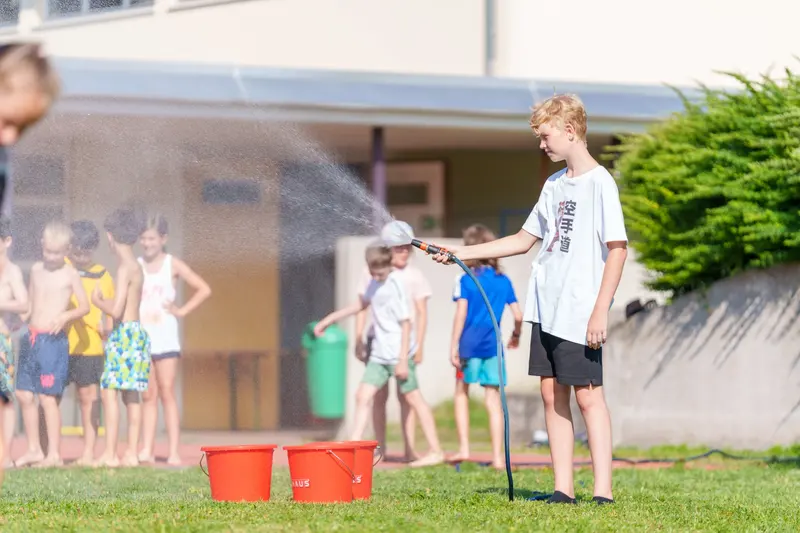 Kind spritzt mit Schlauch Wasser auf Kinder mit Eimern