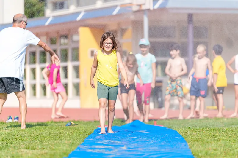 Kind läuft barfuß über blaue Plane, im Hintergrund weitere Kinder