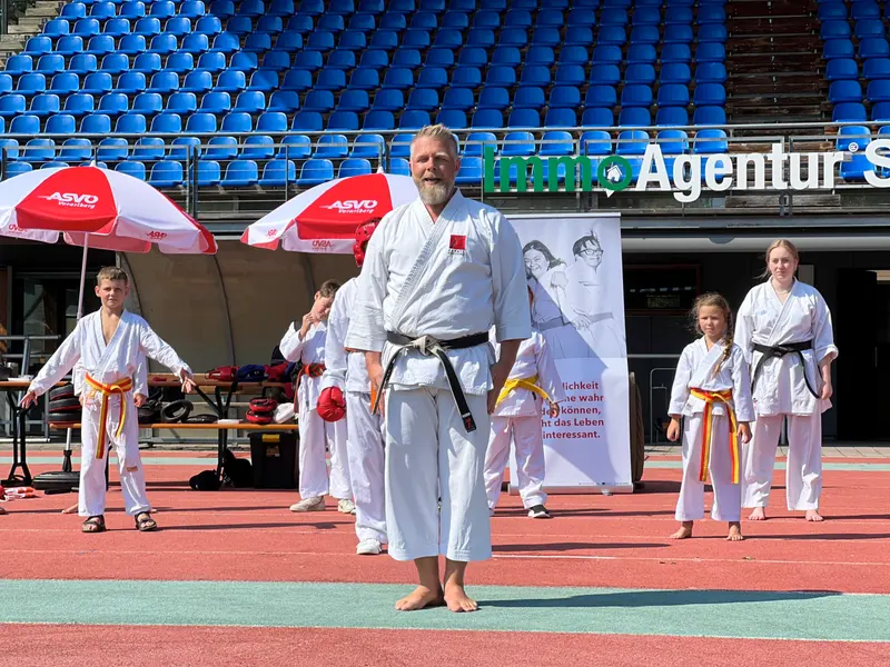Erwachsener in Karategi demonstriert Stellung vor Sonnenschirmen im Stadion