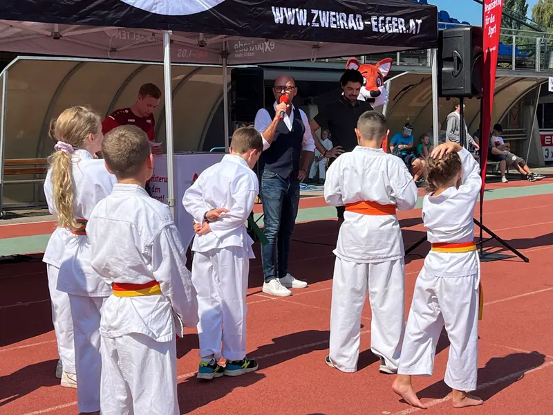 Kinder in Karategi stehen vor Zelt mit Werbebanner