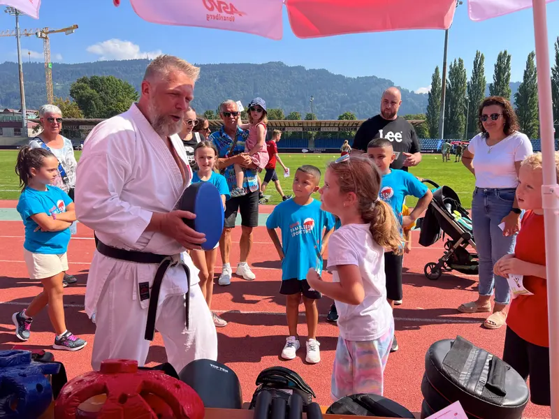 Erwachsener in Karategi spricht mit Kindern in blauen Shirts