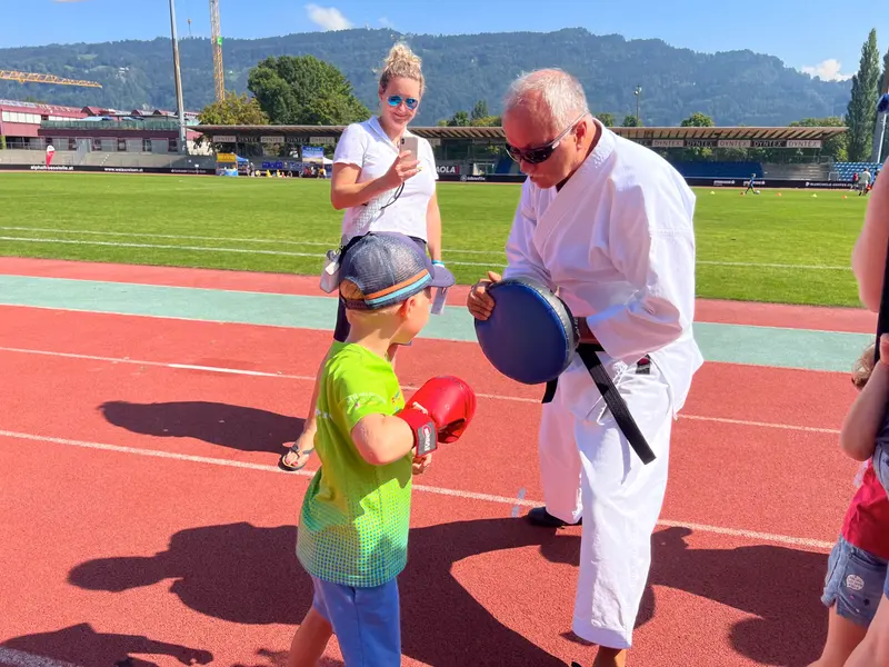 Erwachsener in Karategi hält Boxpratzen für Kind im grünen Shirt