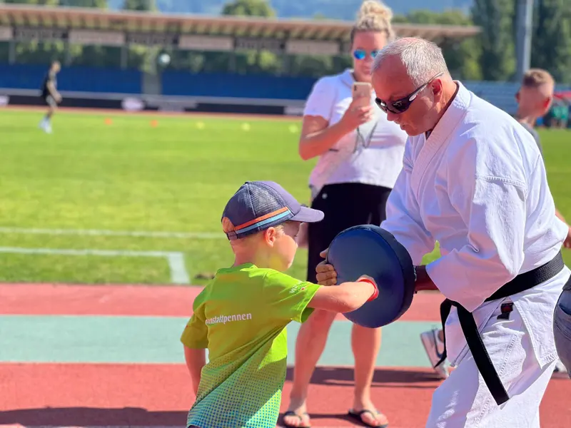 Erwachsener hält Boxpratzen für Kind mit Kappe im Stadion