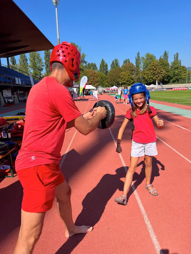 Trainer in rotem Shirt hält Boxpratzen für Kind mit Helm