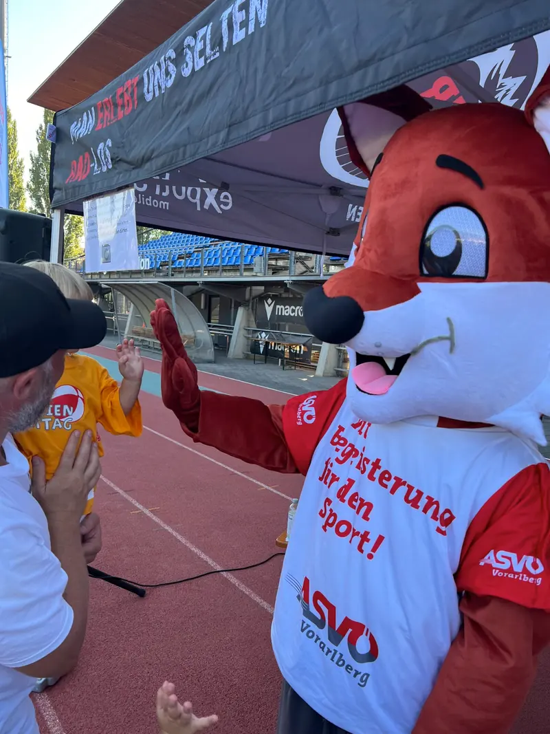 Erwachsener begrüßt Vereinsmaskottchen mit Handschlag im Stadion