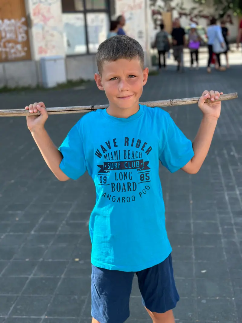 Kind trägt einen Stock über den Schultern, blaues T-Shirt