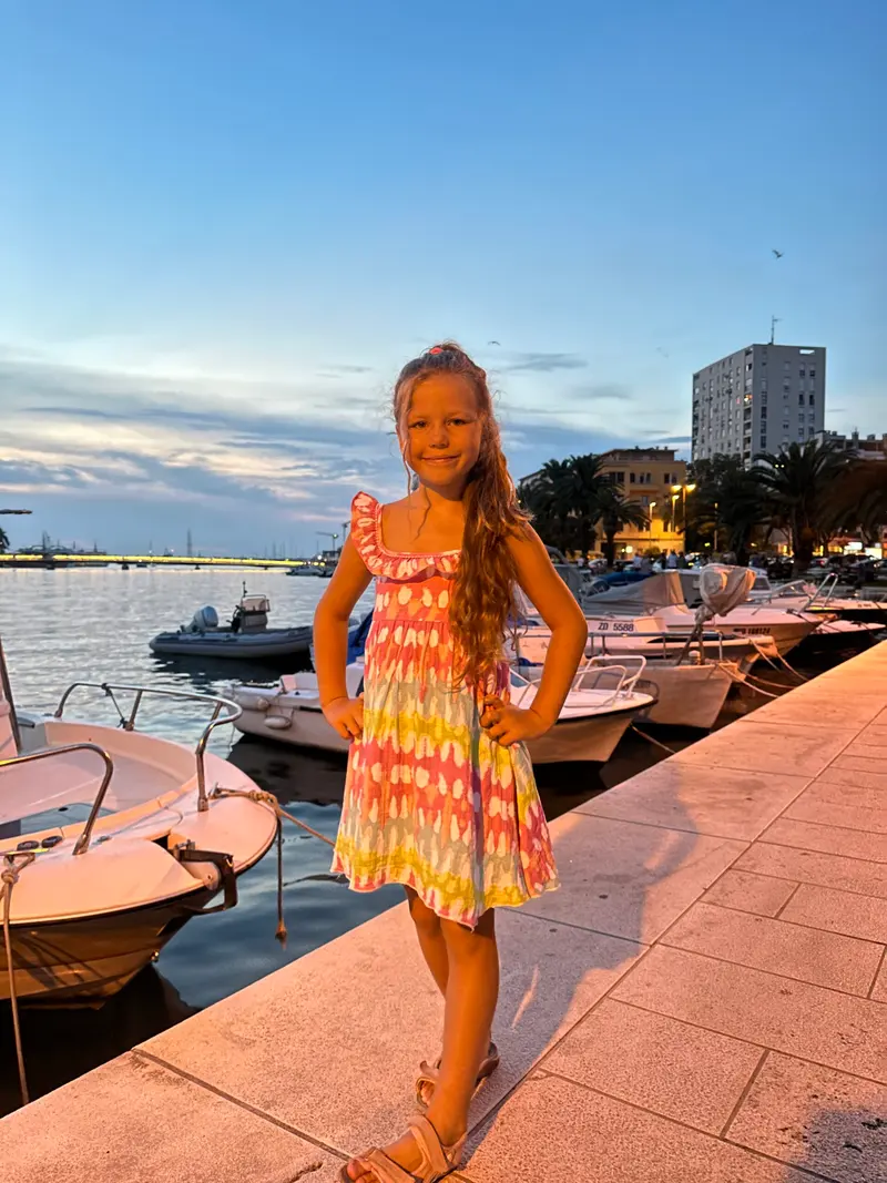Kind im Sommerkleid steht an einem Bootssteg