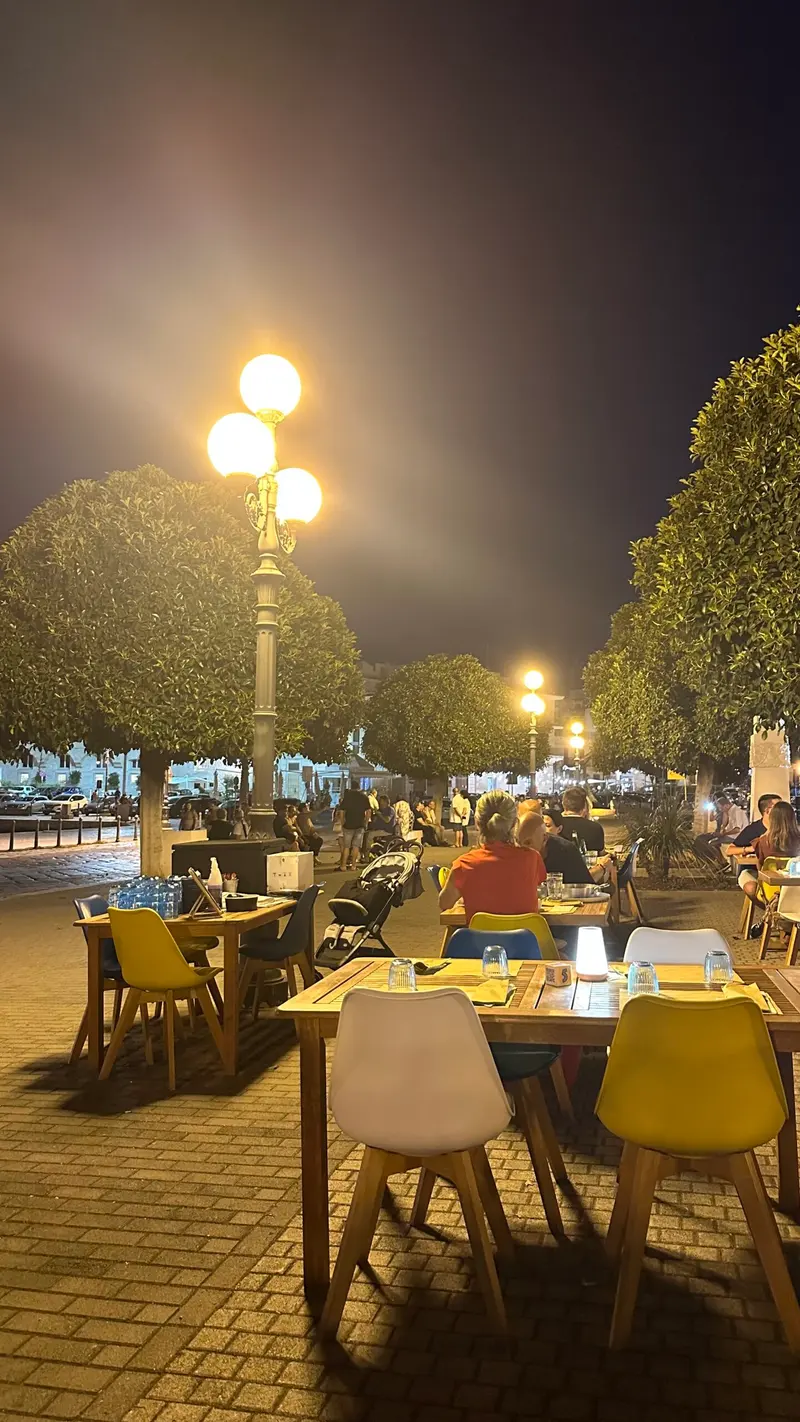 Personen sitzen abends an Tischen entlang einer beleuchteten Promenade
