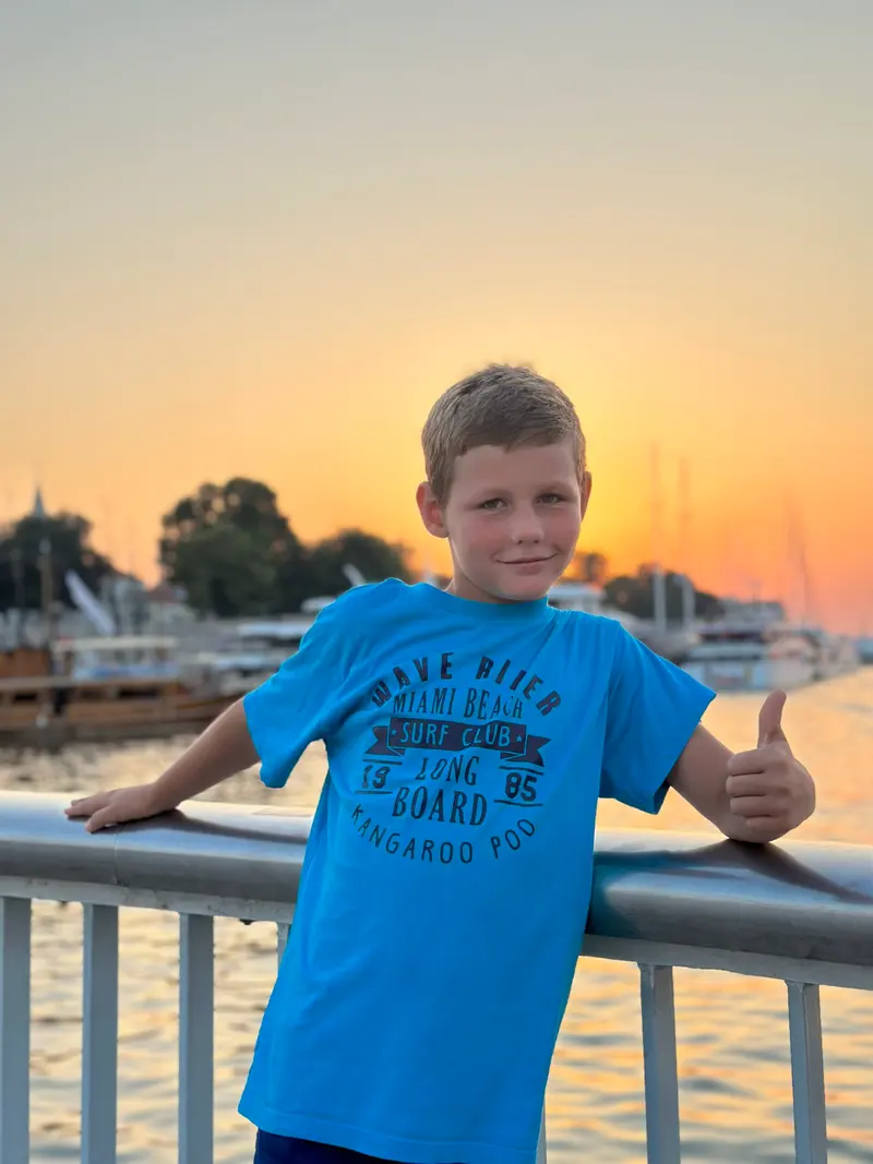 Kind zeigt Daumen hoch auf einem Boot, blaues T-Shirt
