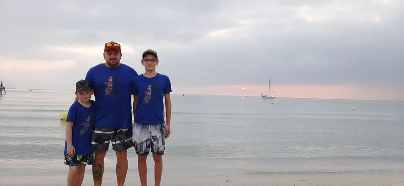 Zwei Personen stehen am Strand bei Sonnenuntergang in gleichen T-Shirts