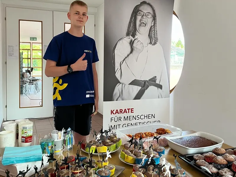 Jugendlicher zeigt Daumen hoch neben Plakat zu inklusivem Karate