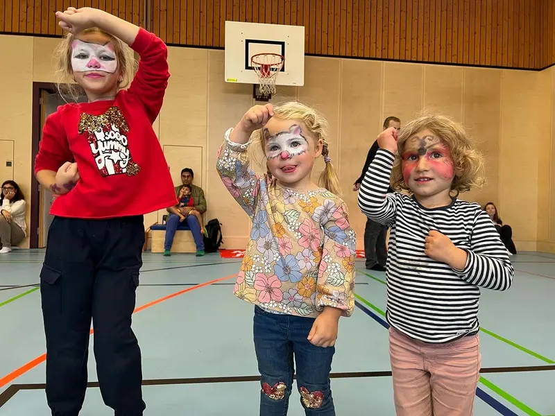 Kinder mit bunt geschminkten Gesichtern posieren in der Halle