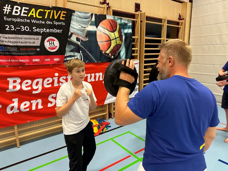 Trainer hält Pratzen, Kind übt Schlagtechnik in der Halle