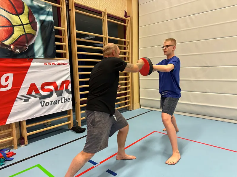 Trainer hält Pratze, Kind in blauem Shirt übt Schlag