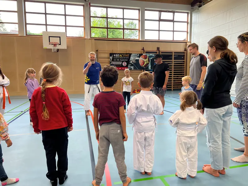 Trainer spricht mit Mikrofon vor Gruppe in der Turnhalle