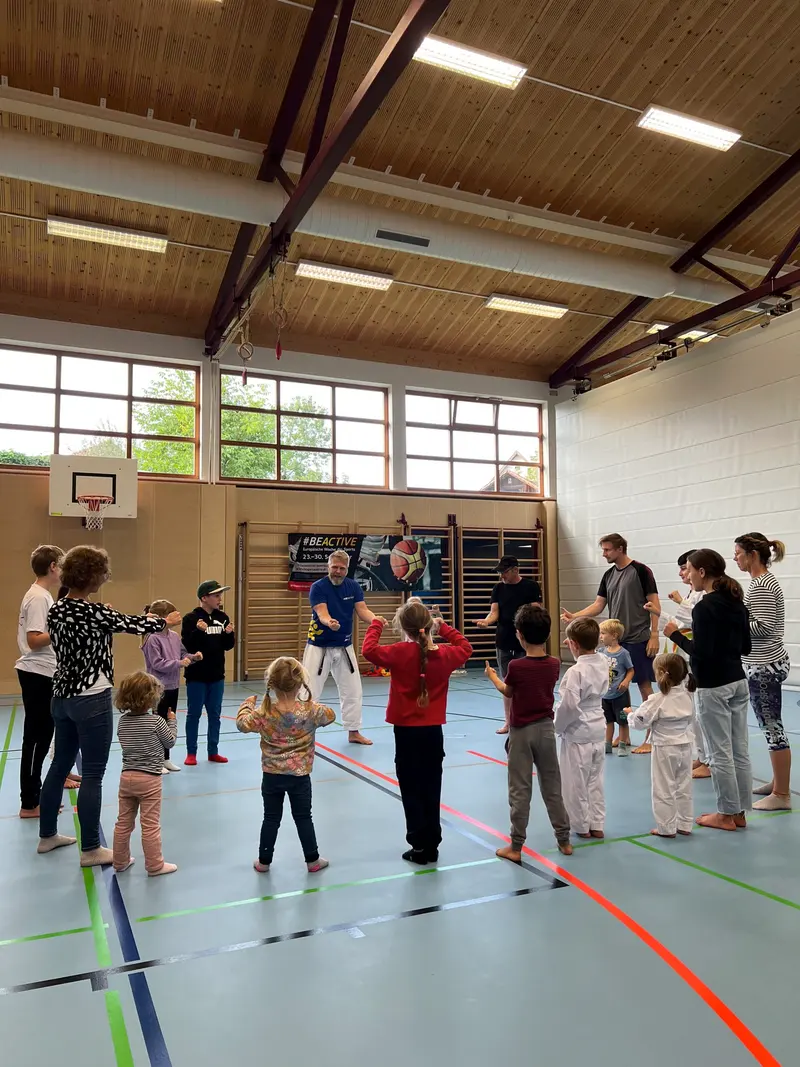 Gruppe aus Kindern und Erwachsenen bildet Kreis in der Halle