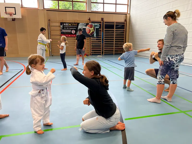 Erwachsene kniet vor Kind im Karategi und übt Schlagtechnik