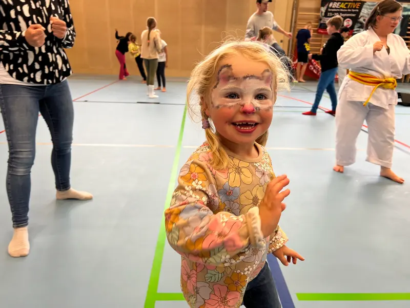 Kind mit geschminktem Gesicht klatscht in der Halle