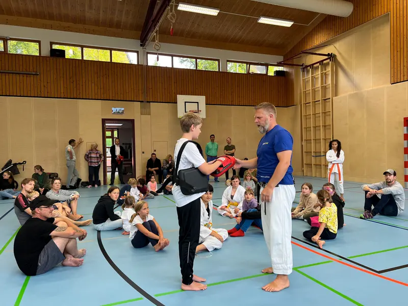 Gruppe sitzt am Hallenrand, zwei Personen stehen im Gespräch