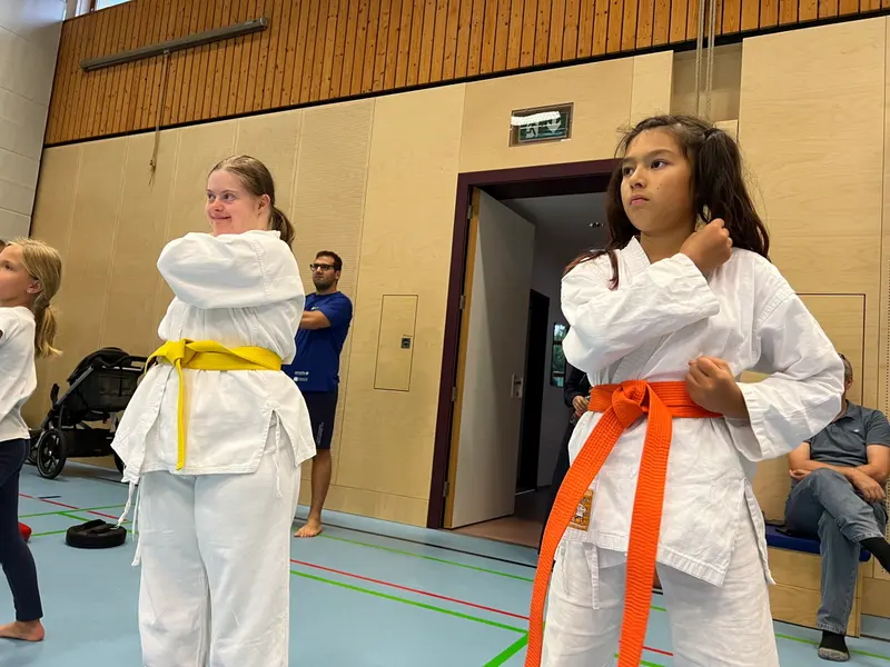 Kinder im Karategi binden ihren Gürtel in der Halle