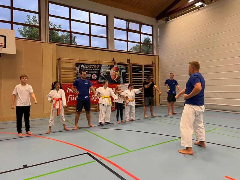 Kinder im Karategi stehen in Reihe, Trainer spricht