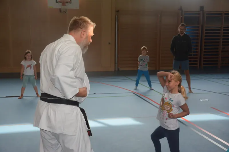 Trainer in Karategi und Kind stehen sich in der Halle gegenüber