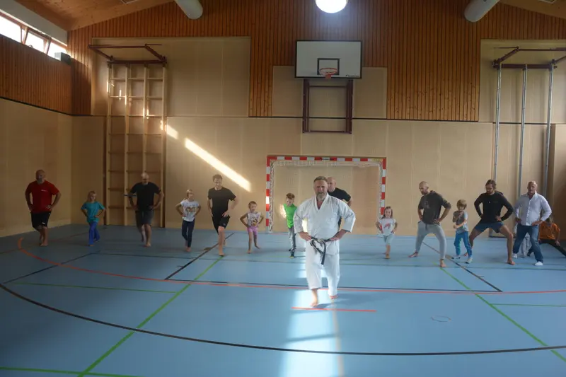 Trainer in Karategi steht zwischen laufenden Kindern und Erwachsenen