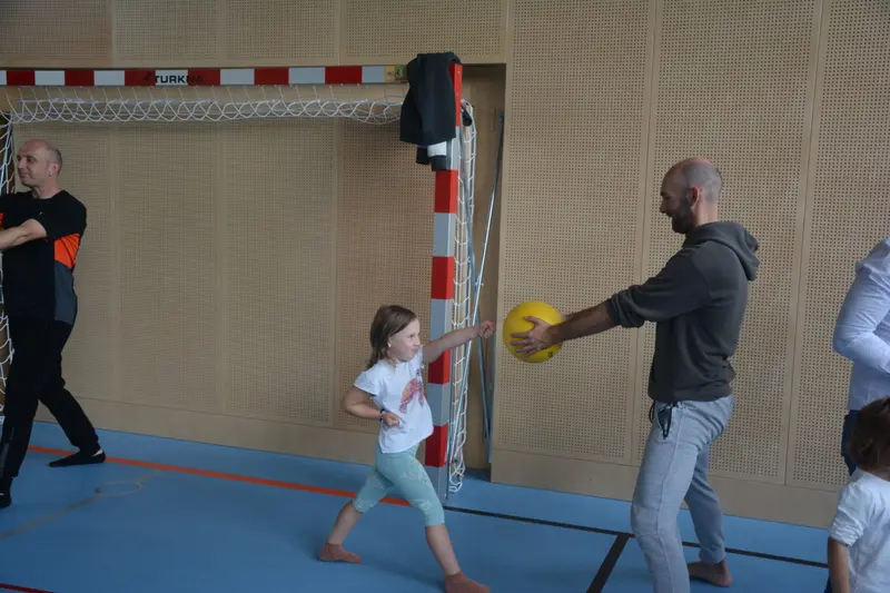 Kind schlägt gegen einen Ball, gehalten von einem Erwachsenen