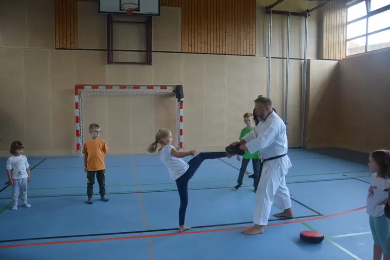 Kind tritt gegen ein Pratzenpolster, gehalten von einer Person in Karategi