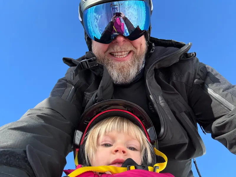 Person mit Skibrille hält Kleinkind auf dem Arm im Schnee