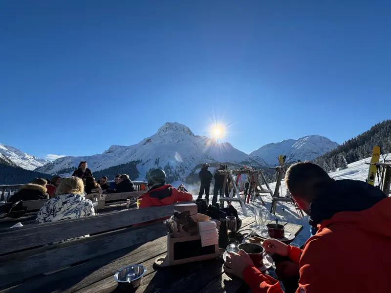 Skipiste mit Personen vor sonnenbeschienener Bergkulisse
