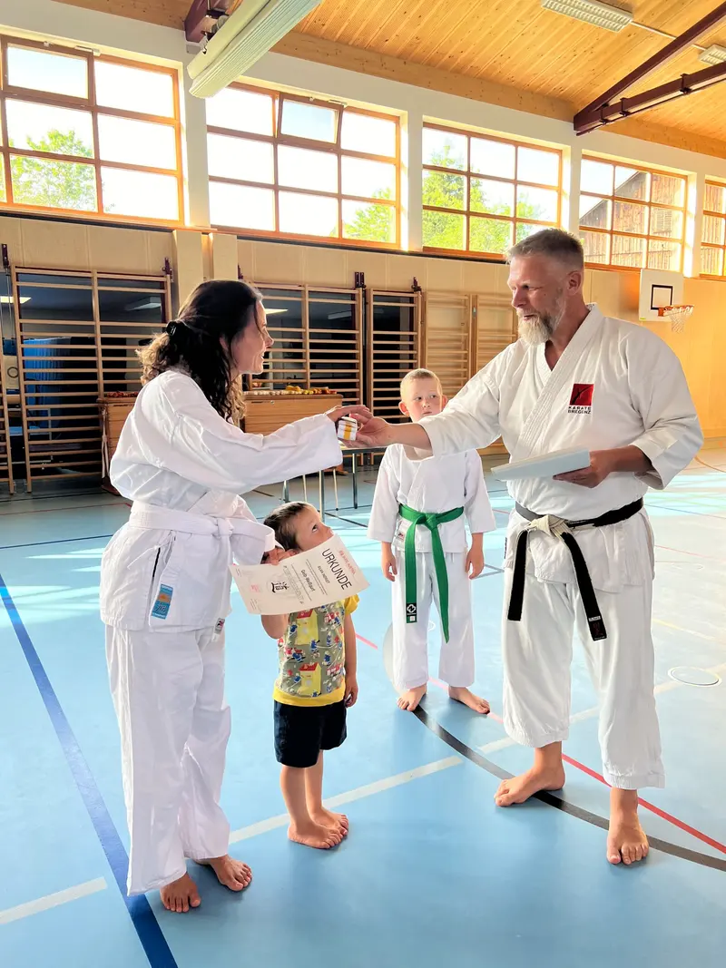 Trainer überreicht Kind mit grünem Gürtel eine Schleife