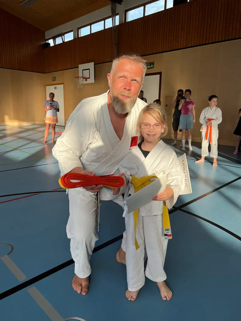 Trainer steht neben Kind mit orange-weißem Gürtel