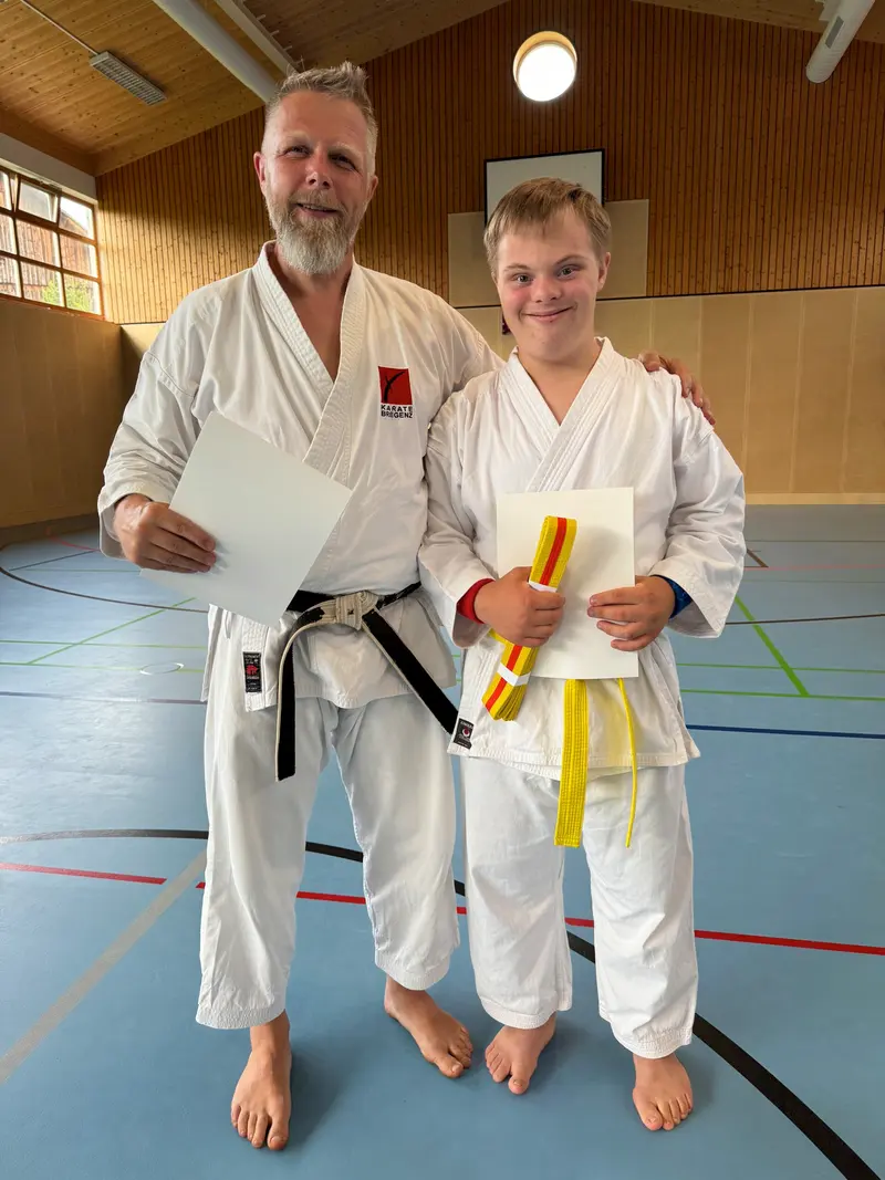 Trainer und Person stehen nebeneinander, Person hält Urkunde in der Hand