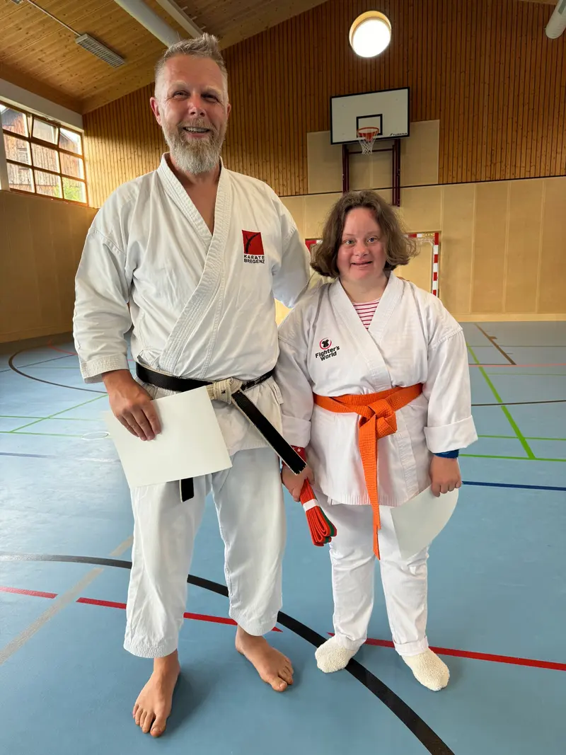 Trainer und Person mit orangem Gürtel stehen nebeneinander