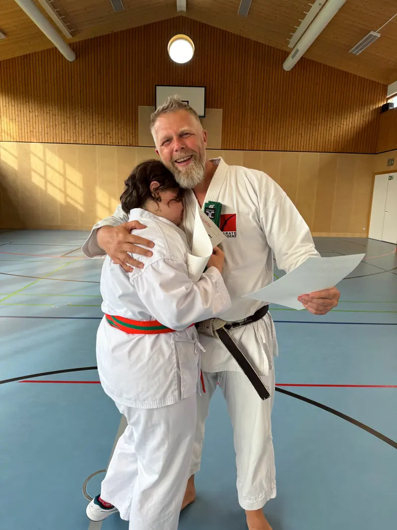 Trainer und Person umarmen sich, orangeroter Gürtel sichtbar
