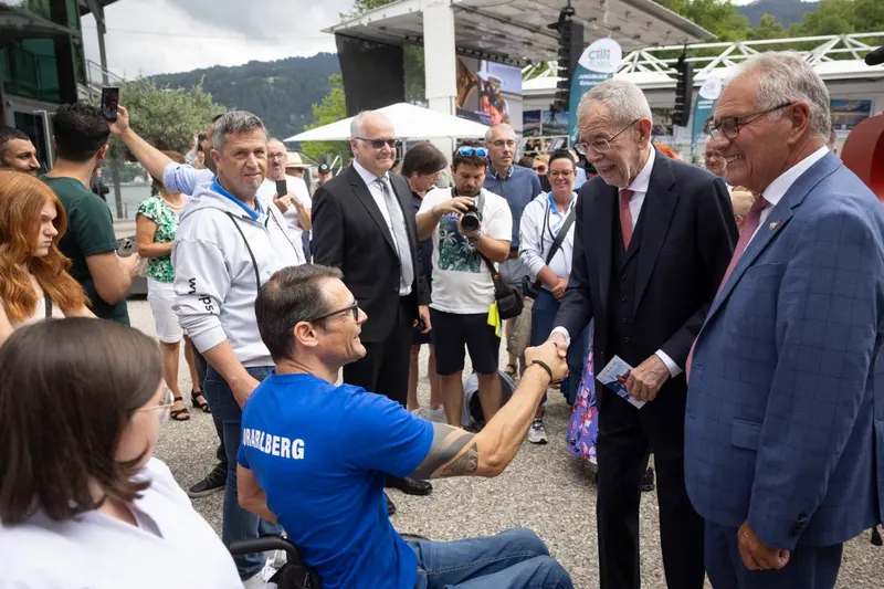 Gruppe steht im Gespräch im Freien, im Hintergrund eine Bühne