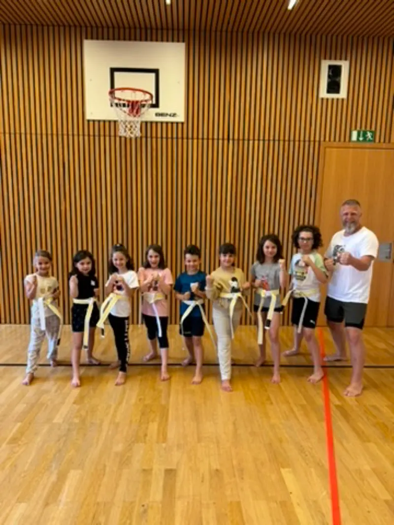 Kinder und Trainer stehen mit Karategi und Gürteln in einer Reihe