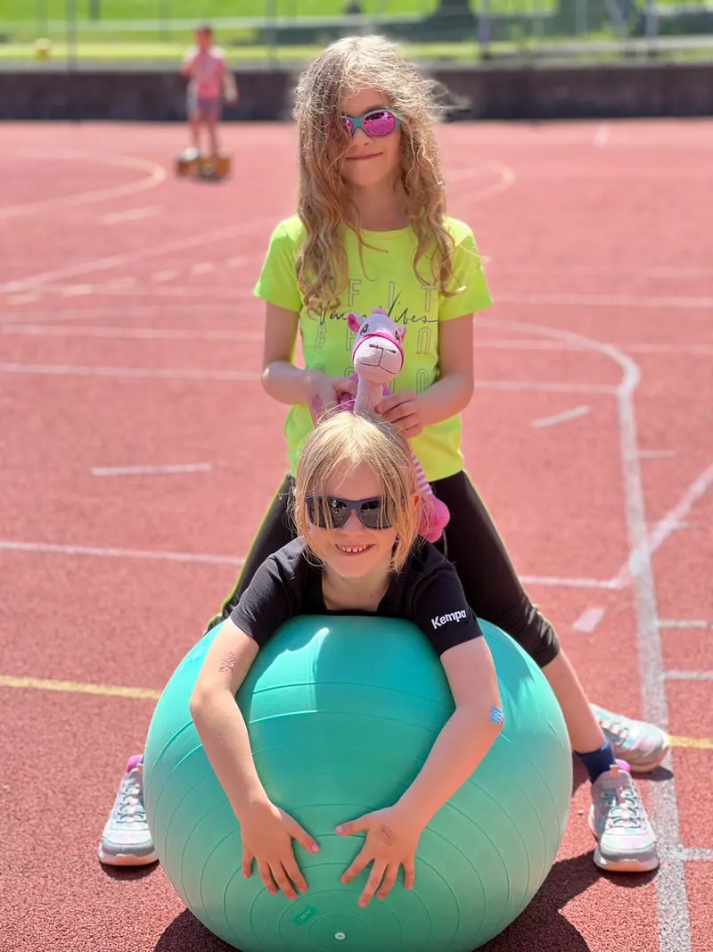 Kind sitzt auf einem Gymnastikball, eine Person hält es fest