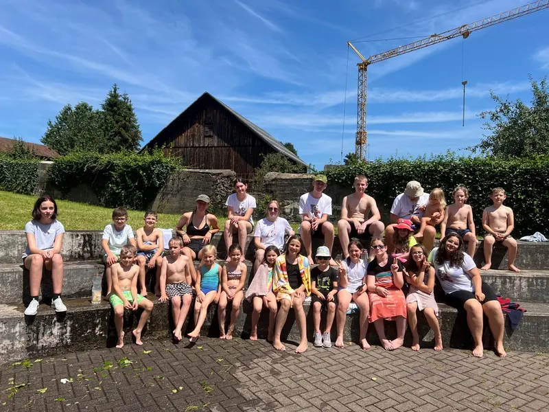 Große Gruppe Kinder und Jugendliche sitzt und steht vor einem Haus