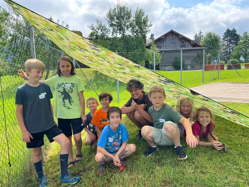 Gruppe Kinder sitzt lächelnd unter einem grünen Sonnensegel im Freien