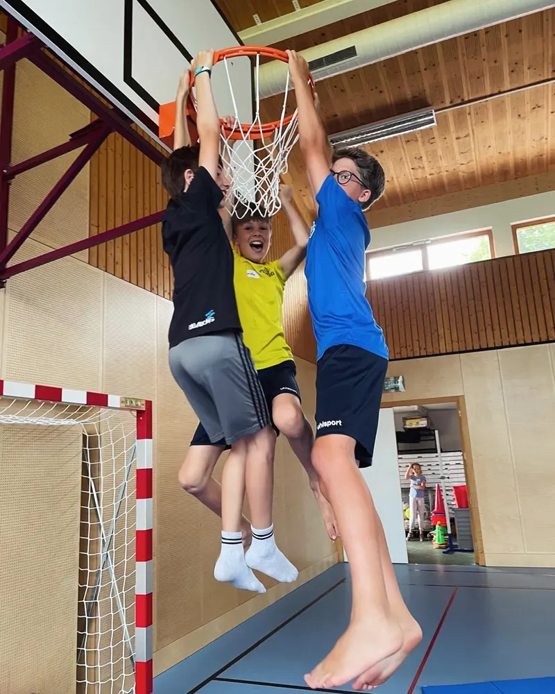 Zwei Kinder springen gemeinsam nach einem Basketballkorb in der Halle