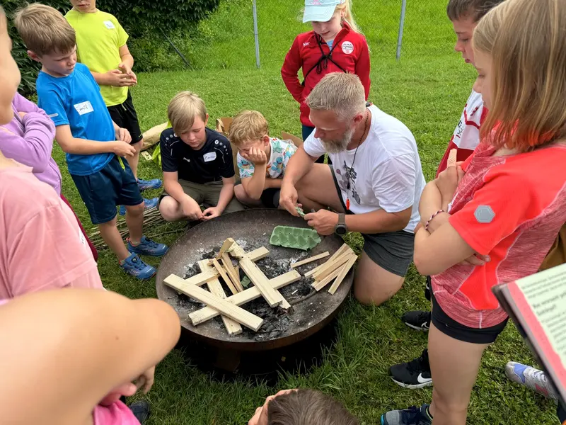 Kinder und Betreuer versammeln sich um eine Feuerschale im Freien