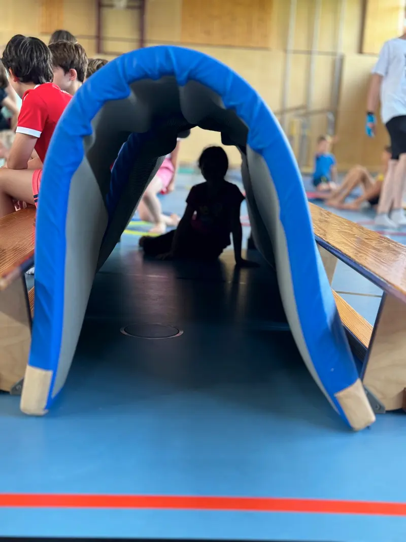 Kind rutscht die blaue Turnrutsche in der Halle hinunter