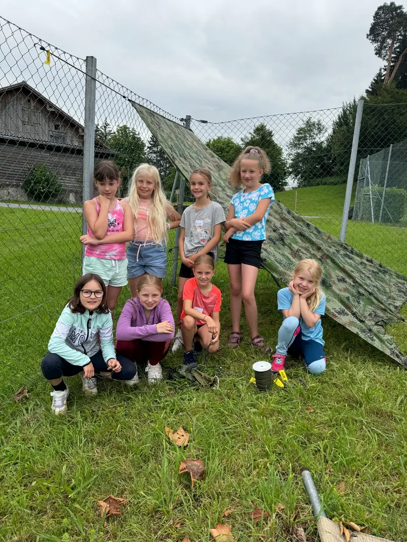 Gruppe Kinder sitzt lächelnd vor einer Kletterwand im Freien